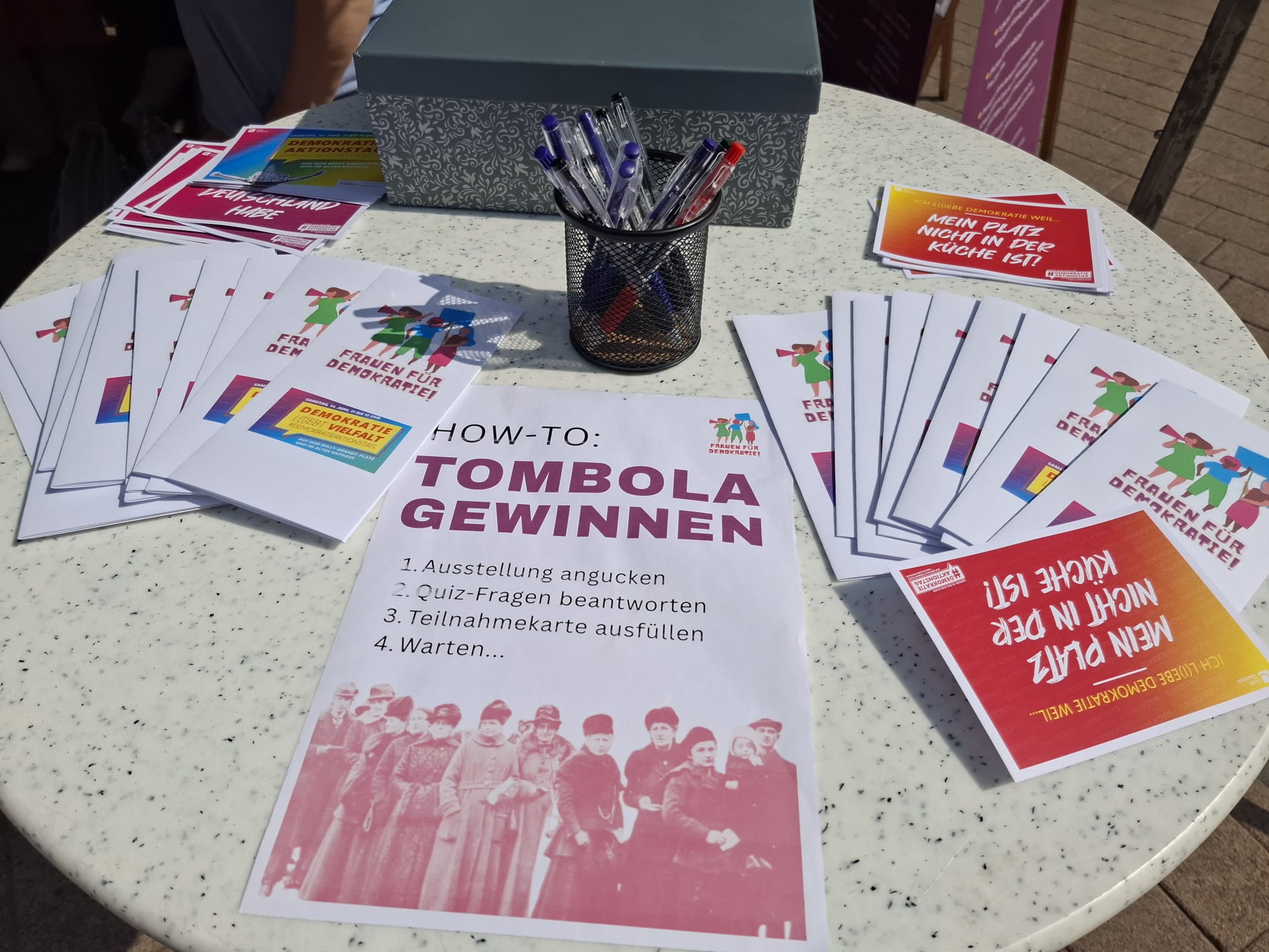 Auf einem Stehtisch liegen Flyer und Teilnahmeunterlagen für ein Quiz im Rahmen der Ausstellung 100 Jahre Frauenwahlrecht der Initiative Frauen für Demokratie